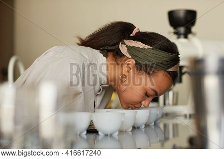 Side View Portrait Of Young Woman Smelling Cofeee During Quality Assesment And Cupping Test In Cafe,