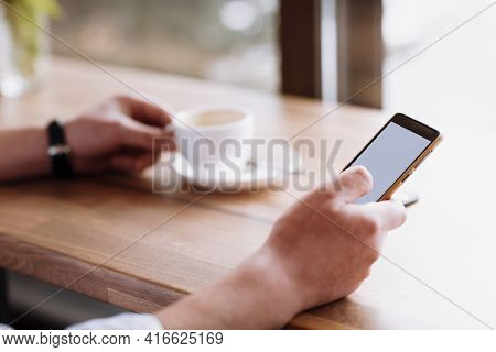 Businessman Hand Holding A Phone With Isolated Screen Against Moke Up And Drink Coffee In The Coffee