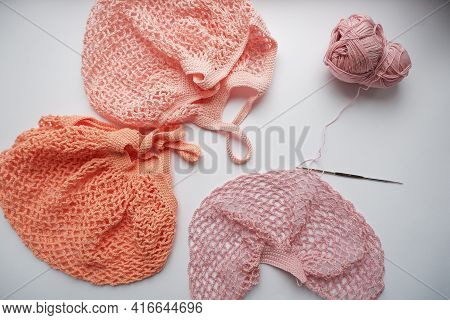 String Bag In The Process Of Knitting. Delicate Pink Mesh Bag, Crochet Hook And Remaining Yarn On A 
