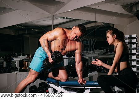 Bodybuiler Couple Trainig Biceps. Personal Trainer Helping Woman Working With Heavy Dumbbells In Gym