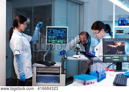 Scientist Analyzing Blood Sample In Vacutainer With Researching Team