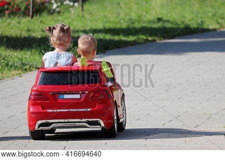 Little Girl And Boy Riding A Toy Car In A Park. Couple Of Kids Having Fun, Children Leisure, Driving