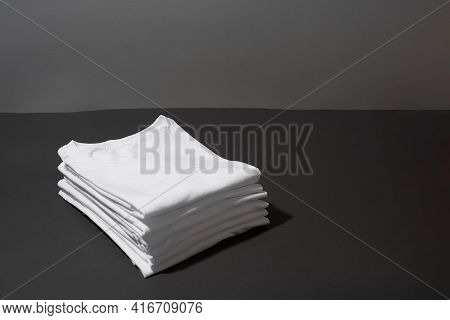 Stack Of Folded White Cotton T Shirts Isolated Over Dark Gray Background. Tees Template. Clothes, Mi