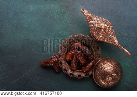 Bronze plate with dates  and aladdin lamp on dark green  painted wooden background  with empty space for text . Flat lay. Ramadan background. Ramadan kareem. 