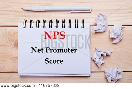 On A Wooden Background, A White Notebook With The Inscription Nps Net Promoter Score, A White Pen An