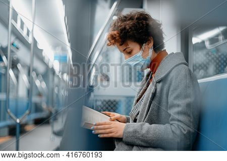 Woman In A Protective Mask Reads A Book On A Subway Train.