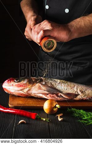 The Cook Prepares Fresh Fish Bighead Carp Sprinkling Pepper. Preparing To Cook Fish Food. Working En