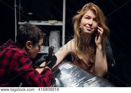 An Experienced Tattoo Artist With A Tattooed Face Fills A Tattoo To Her Client A Girl With Red Hair 