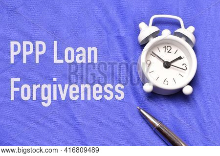 Top View Of Clock, Pen Over Blue Background Written With Ppp Loan Forgiveness.