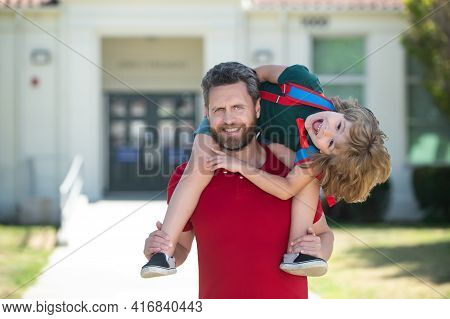 Teacher In T-shirt And Cute Schoolboy With Backpack Near School Park. Man And Excited Amazed Kid Pig