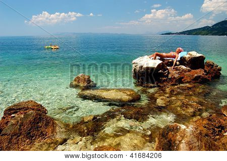 Young girl is sunbathing on a rocky beach in Croatia