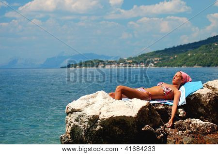 Young girl is sunbathing on a rocky beach in Croatia