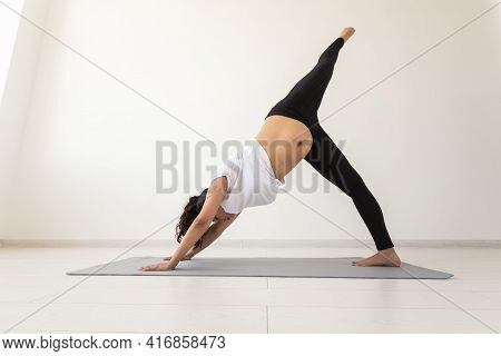 Young Flexible Pregnant Woman Doing Gymnastics On Rug On The Floor On White Background. The Concept 