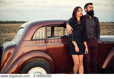 Bearded Brunette In A Shirt And Trousers With Suspenders Hugs A Slender Young Girl With Long Hair In