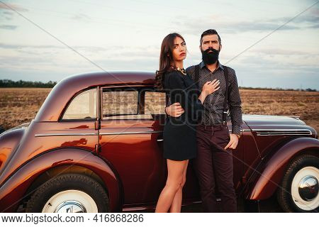 Bearded Brunette In A Shirt And Trousers With Suspenders Hugs A Slender Young Girl With Long Hair In