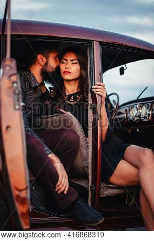 Brutal Bearded Brunette Man In A Shirt And Trousers With Suspenders Kisses A Slender Young Girl With