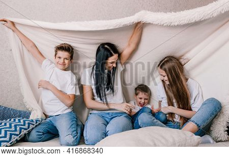 Happy Family Mom And Small Children Laughing Merrily Sitting On The Sofa Covered With A White Blanke