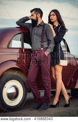 Stylish Bearded Brunette Man In A Shirt And Trousers With Suspenders Hugs A Slender Young Girl With 