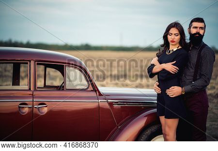 Stylish Bearded Brunette Man In A Shirt And Trousers With Suspenders Hugs A Slender Young Girl With 