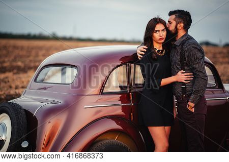 Stylish Bearded Brunette Man In A Shirt And Trousers With Suspenders Hugs A Slender Young Girl With 