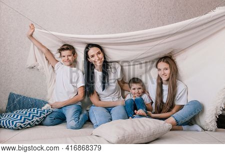 Happy Family Mom And Small Children Laughing Merrily Sitting On The Sofa Covered With A White Blanke