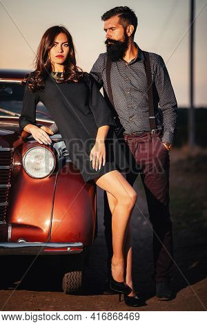 Bearded Brunette Man In A Shirt And Trousers With Suspenders Hugs A Slender Young Girl With Long Hai
