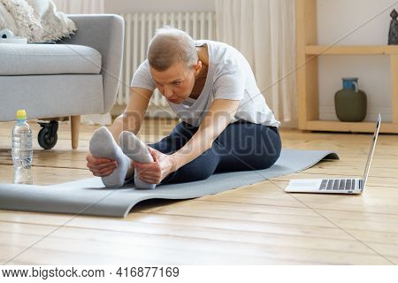 Senior Woman Stretching, Online Training With Laptop In Living Room. Exercising For Health. Well-bei
