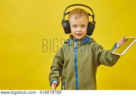 A Boy Wearing Wireless Headphones With A Digital Tablet On A Yellow Background. Modern Children And 