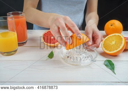 Young Woman Squeezes Orange Juice Using A Manual Glass Juicer.
