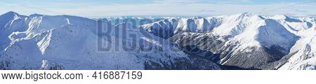 Magnificent Panoramic Shot Of Mountain Peaks Covered In Snow During The Winter Season. A Blue Sky Wi