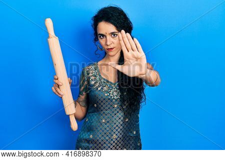 Young woman wearing bindi and traditional kurta dress holding kneading roll with open hand doing stop sign with serious and confident expression, defense gesture 