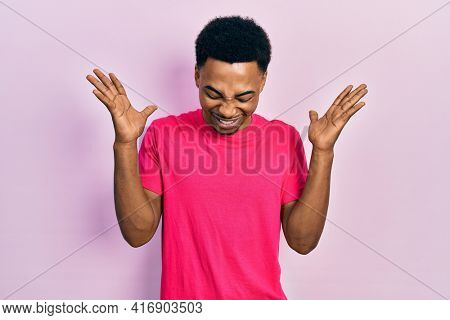 Young african american man wearing casua t shirt celebrating mad and crazy for success with arms raised and closed eyes screaming excited. winner concept 