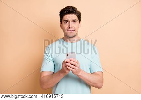 Portrait Of Nice Worried Guy Blogger Influenzer Using Gadget Biting Lip Dislike Isolated Over Beige 