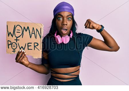 Young african american girl wearing sportswear holding woman power banner afraid and shocked with surprise and amazed expression, fear and excited face. 