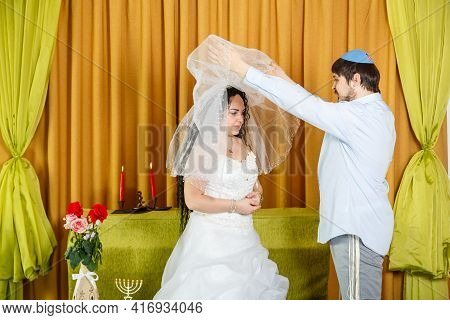 During The Chuppah Ceremony At A Synagogue Wedding, The Groom Lifts The Veil From The Bride's Face. 