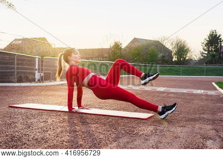 Young Fitness Woman In Red Sportswear Doing Reverse Plank Knee Tuck Exercise On The Mat. Outdoors Wo