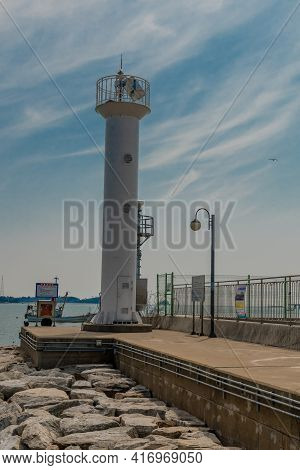 Pyeongtaek, South Korea; April 6, 2021: White Lighthouse On End Of Concrete Pier Under Blue Sky With