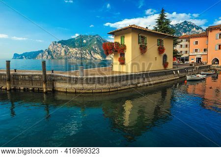 Moored Wooden Boats And Colorful Cute Building Decorated With Flowers On The Pier. Small Harbor And 