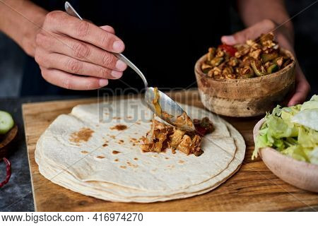 a young caucasian man fills a durum or a burrito, with chicken meat cooked with different vegetables such as onion or red and green pepper