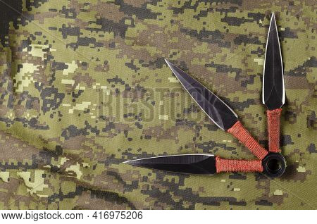 Black Throwing Knives On Camouflage Cloth. Three Special Knives With Red Handles Crossed. Military T