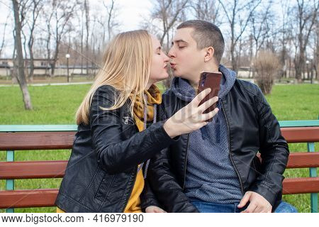 Husband And Wife Take A Selfie While Sitting On A Swing In The Park. Happy Couple Taking Pictures Of