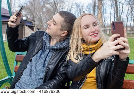 Husband And Wife Take A Selfie While Sitting On A Swing In The Park. Happy Couple Taking Pictures Of