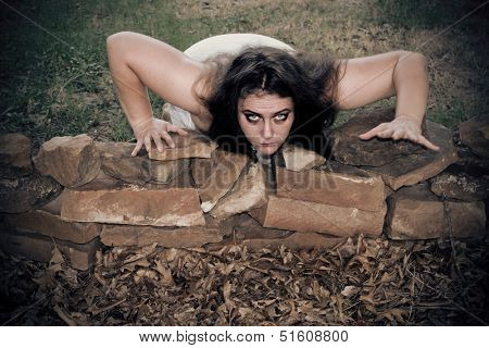 A woman zombie crawls out with a menacing look
