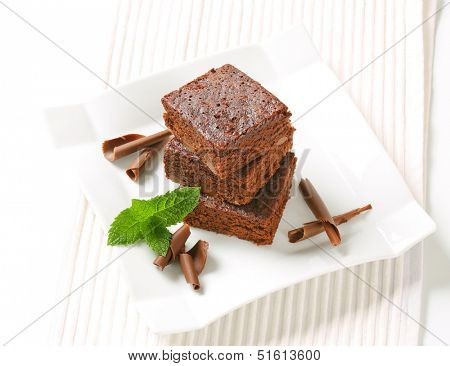 three pieces of smooth brownies with chocolate curls on a square plate
