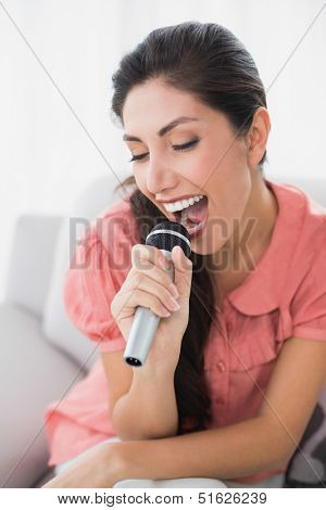 Brunette sitting on her sofa singing into microphone at home in the sitting room