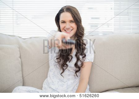 Smiling young woman holding remote sitting on a cosy couch in bright living room