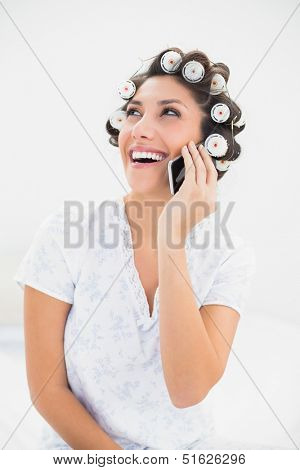 Laughing brunette in hair rollers on the phone on bed at home in bedroom