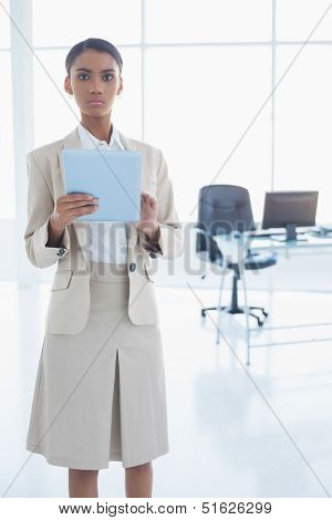 Stern elegant businesswoman in bright office using her tablet