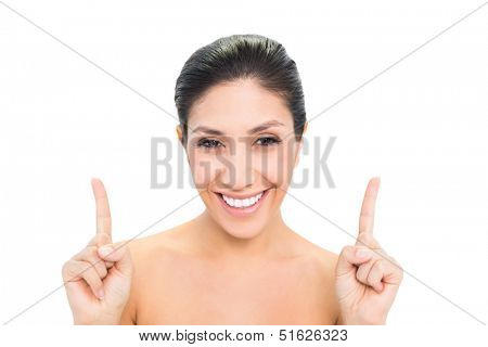 Smiling brunette pointing up with both hands on white background