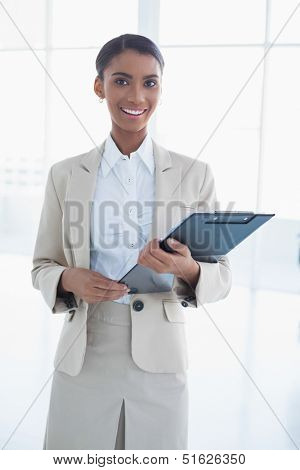 Cheerful elegant businesswoman in bright office holding clipboard